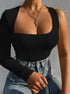 Woman in a black one-shoulder top with long sleeve, wearing layered necklaces and blue high-waisted jeans.