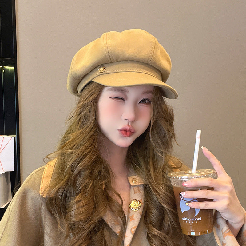 Woman in beige newsboy cap making kiss face while holding iced coffee, wearing matching beige outfit