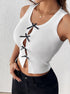 Side view of a woman in a white sleeveless ribbed crop top featuring black bows along the cutout, styled with black pants and gold accessories.