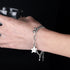 A stylish silver chain bracelet with a star-shaped charm that reads "Luck," worn on a hand holding a black cup.