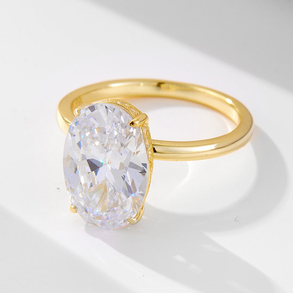 A gold solitaire ring with large oval-cut diamond center stone in prong setting, displayed on white surface with soft shadow