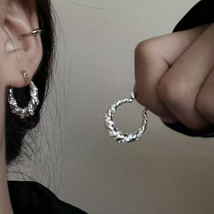 Silver twisted hoop earrings with crystal accents shown worn and held to display pattern