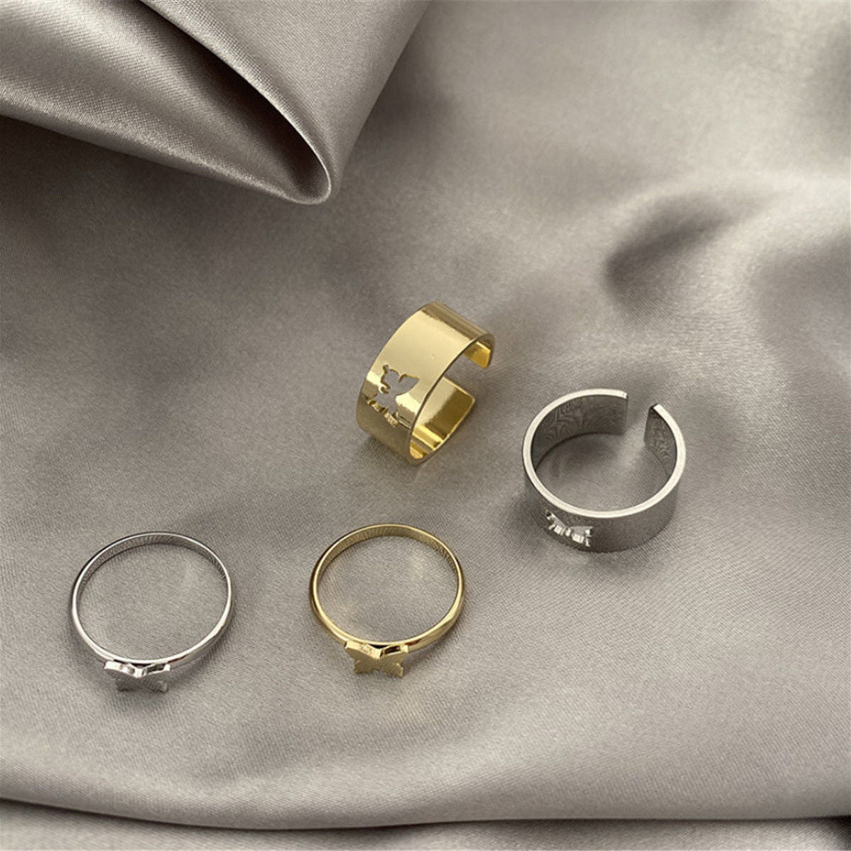 Four butterfly rings displayed on gray silk: wide bands and thin bands in gold and silver finishes