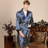 Man standing beside antique table wearing navy striped silk robe. Close-up shows wraparound style with matching belt and pink roses in vase