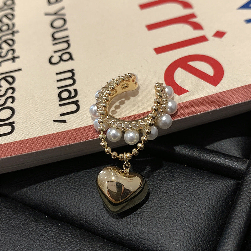 Pearl and gold ear cuff with dangling heart charm displayed on book page with black leather surface