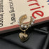 Pearl and gold ear cuff with dangling heart charm displayed on book page with black leather surface