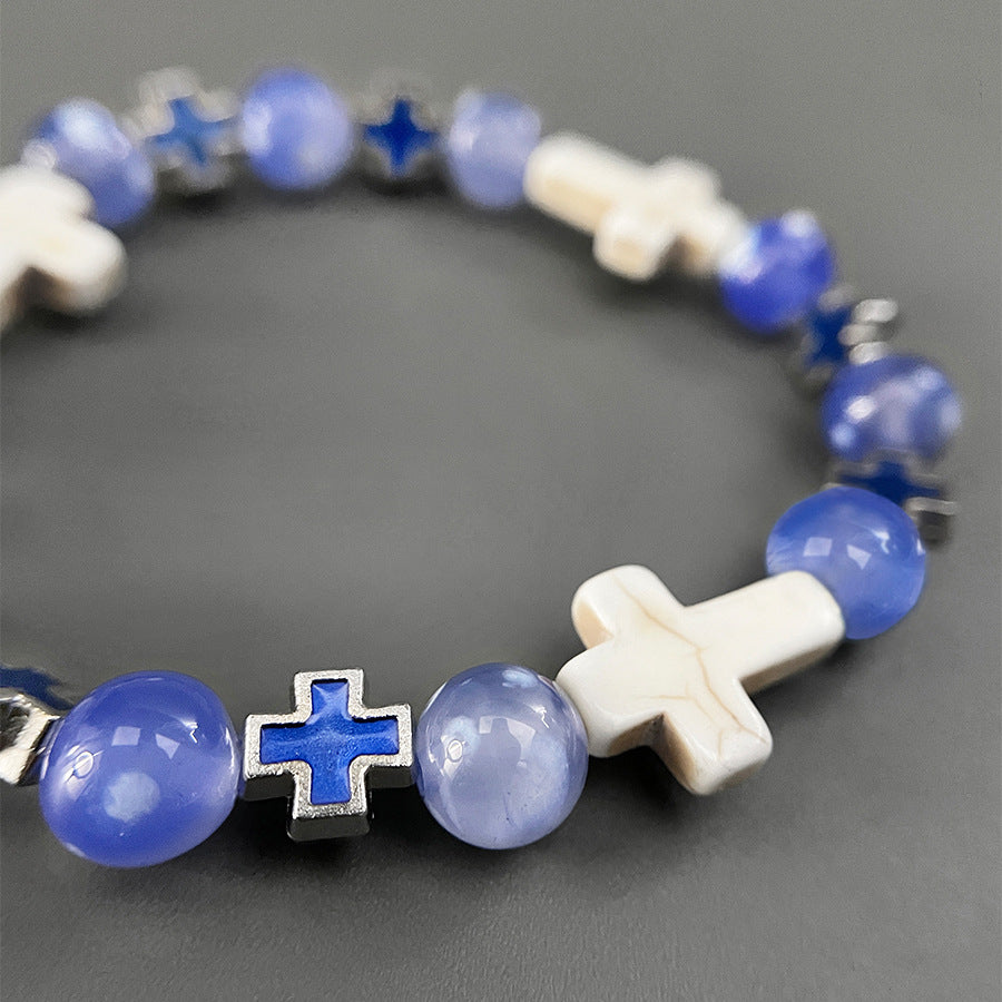 A detailed view of a beaded bracelet featuring blue gemstone beads, white cross-shaped beads, and metallic blue cross accents on a gray background.