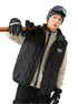 Male model carrying ski equipment, wearing black puffer vest over cream ribbed sweater, gray beanie, ski goggles, gloves with Skiing logo