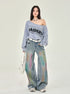 A model in gray Raiders sweatshirt styled off-shoulder, tie-dye wide-leg jeans, white accessories, photographed in studio setting