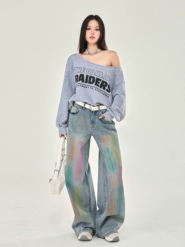 A model in gray Raiders sweatshirt styled off-shoulder, tie-dye wide-leg jeans, white accessories, photographed in studio setting