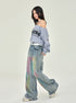 A model in side pose wearing Raiders off-shoulder sweatshirt, watercolor-effect wide-leg jeans, white belt, against neutral backdrop