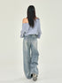 A model photographed from behind in gray off-shoulder sweatshirt, light wash wide-leg jeans, sneakers, studio setting