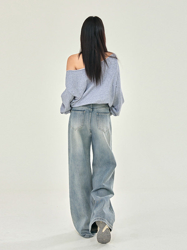 A model photographed from behind in gray off-shoulder sweatshirt, light wash wide-leg jeans, sneakers, studio setting