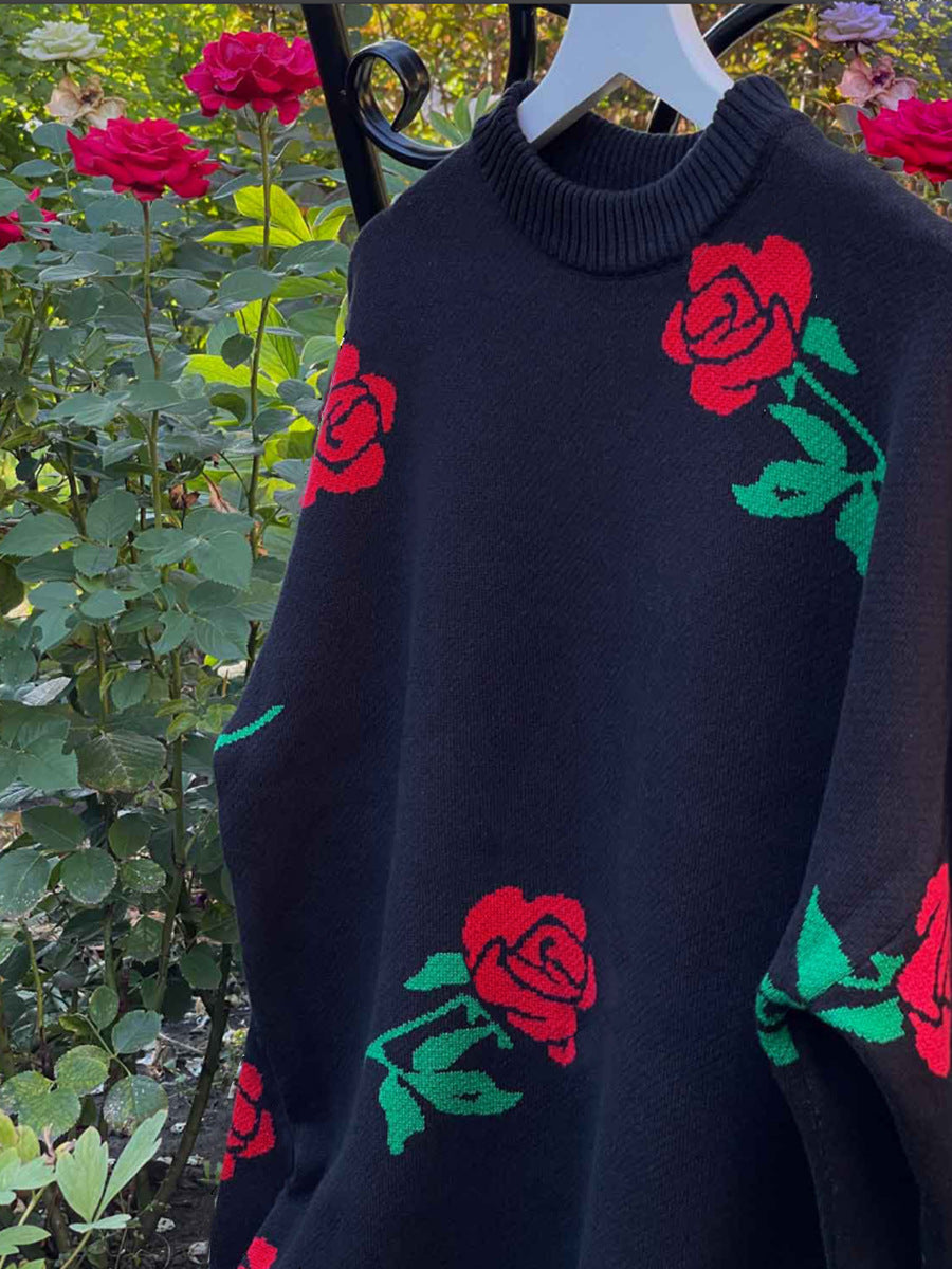 Black sweater with red rose and green leaf pattern hanging against garden backdrop with blooming roses