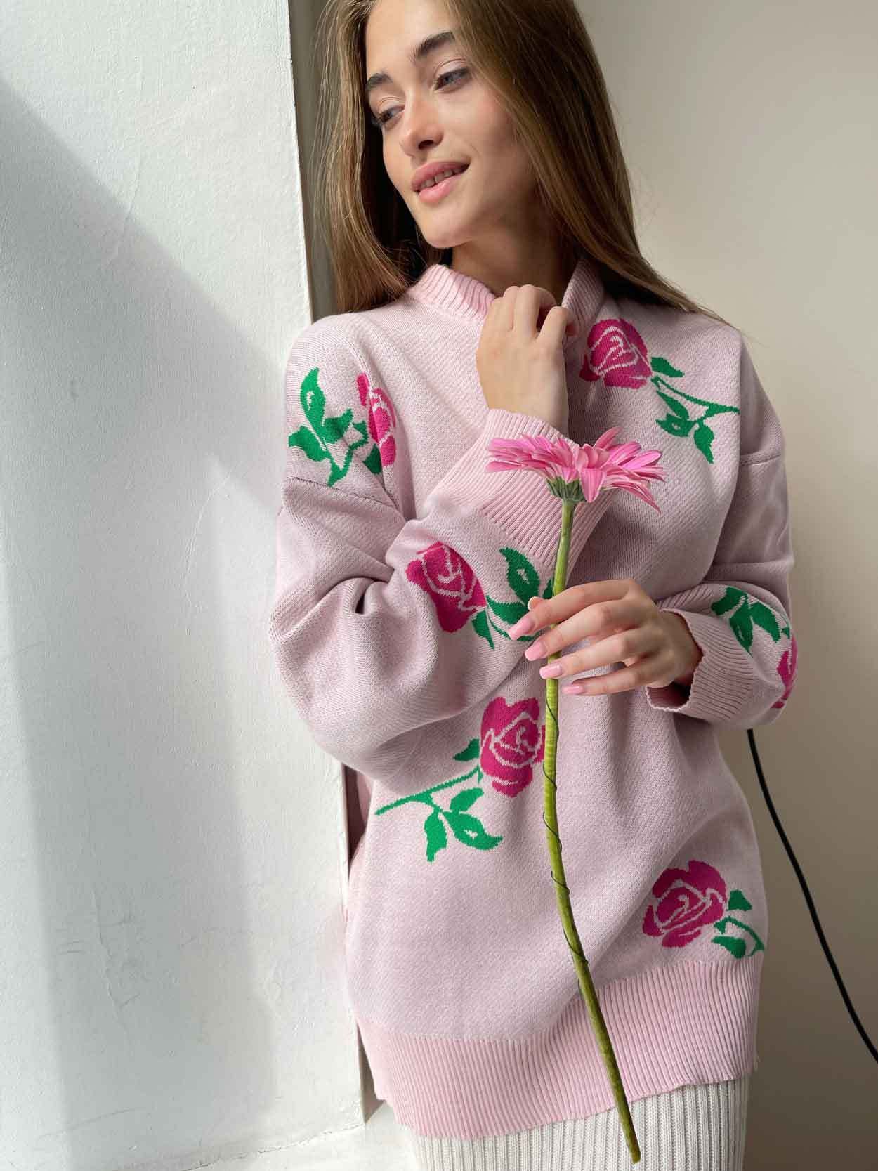 Light pink sweater with rose pattern, model holding pink gerbera daisy in natural lighting