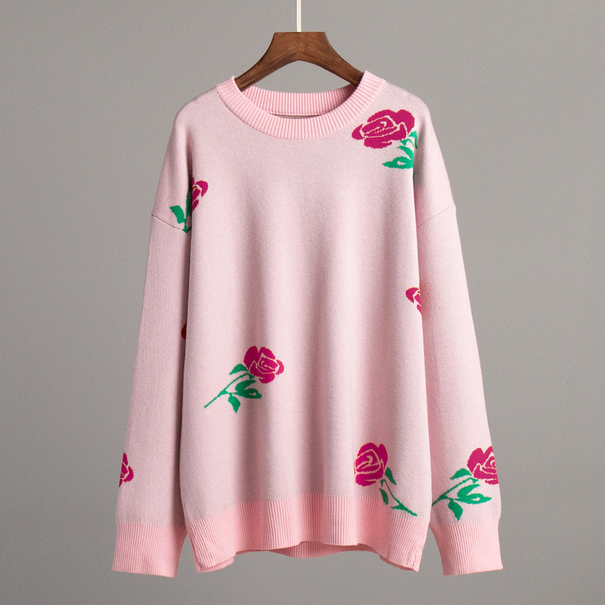 Light pink oversized sweater with rose print and ribbed trim displayed on wooden hanger