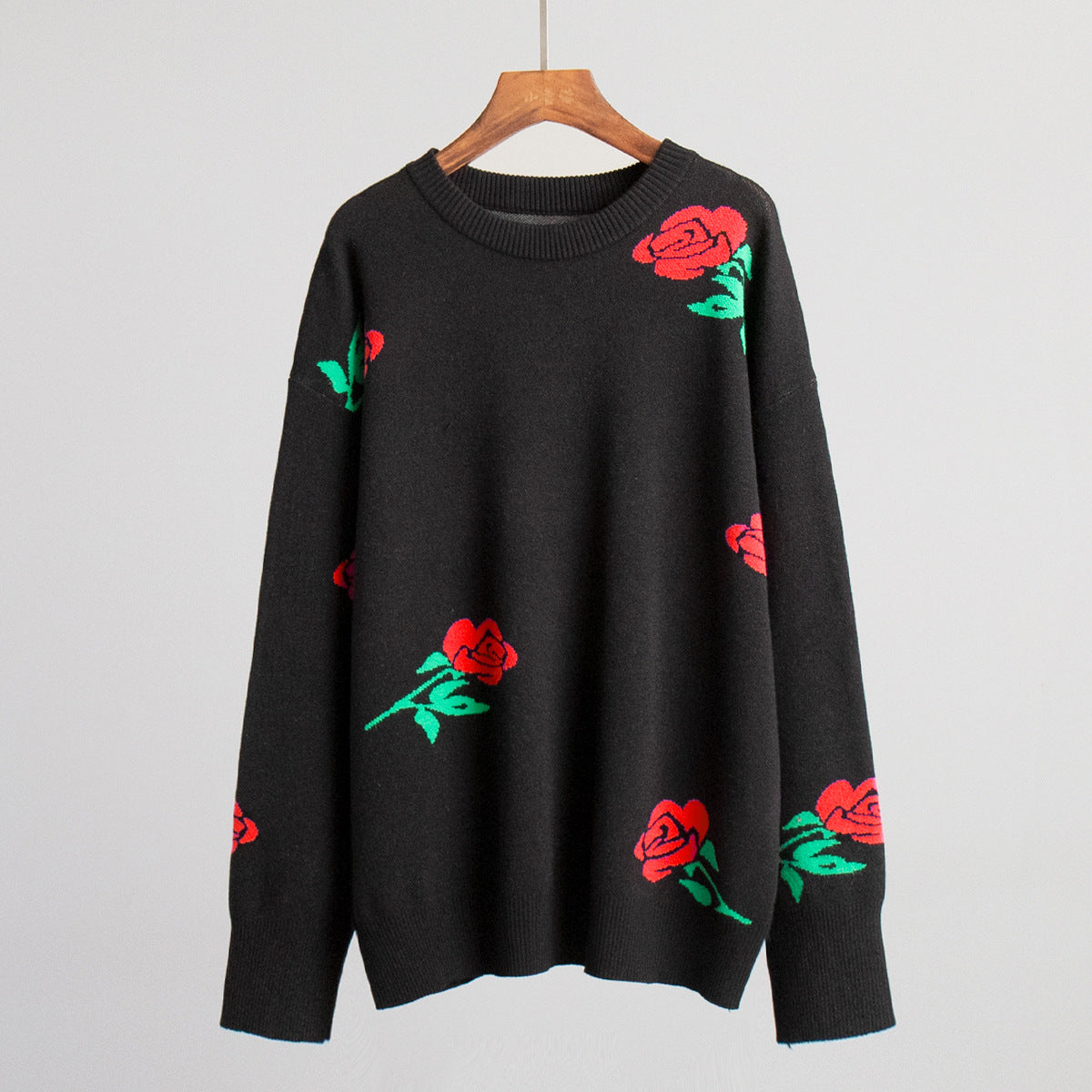 Black knit sweater with red rose pattern displayed on wooden hanger against white background