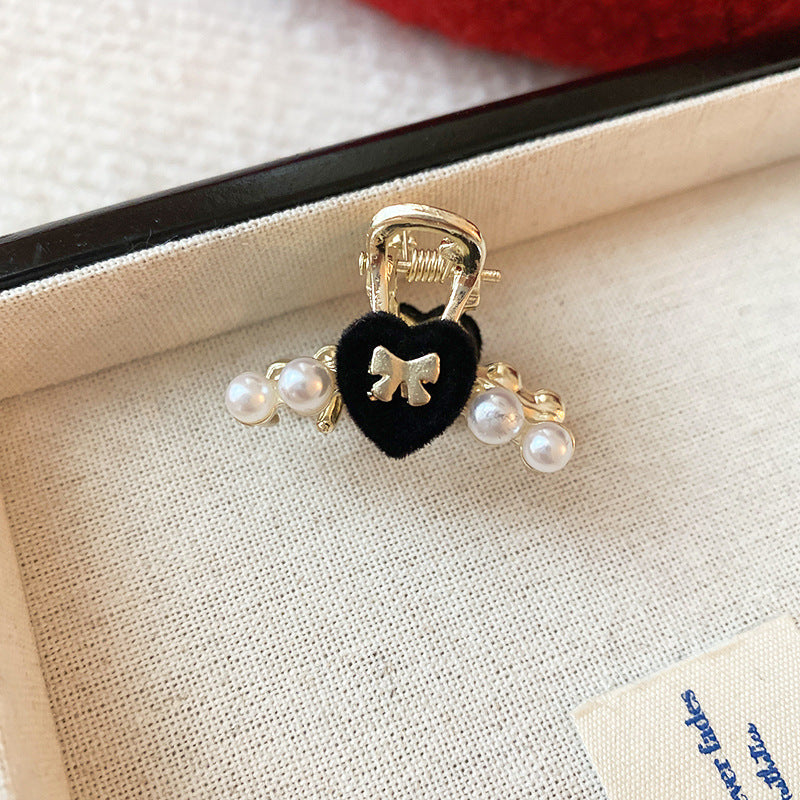  A small gold hair claw featuring a black velvet heart with a gold bow and pearl embellishments on a jewelry box.