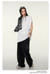 Model with braided hair wearing white oversized t-shirt, black pants, holding gray jacket with white sunglasses