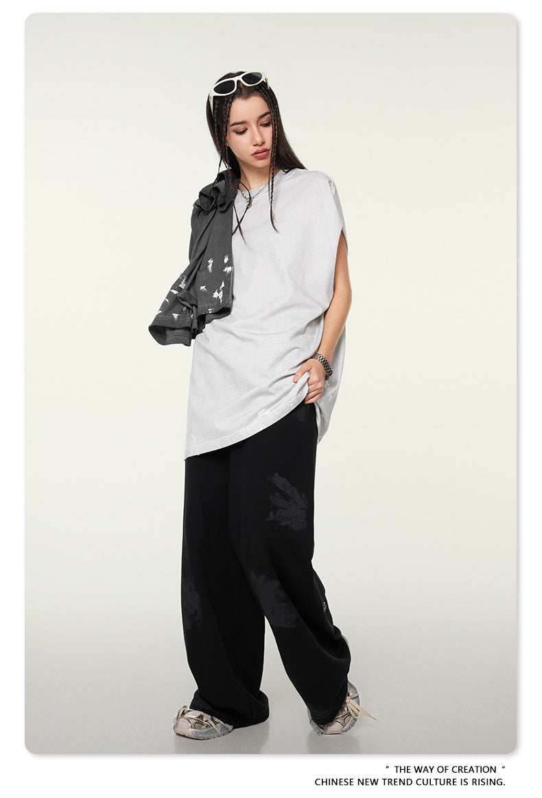 Model with braided hair wearing white oversized t-shirt, black pants, holding gray jacket with white sunglasses