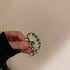 Emerald green gemstone eternity ring with square-cut stones set in a gold-toned metal, showcasing a sparkling circular design