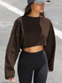 A woman wearing a brown cropped sweatshirt with wide sleeves and black high-waisted leggings stands outdoors with gray baseball cap