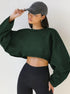 A woman wearing a forest green cropped sweatshirt and black leggings touches her charcoal baseball cap against a neutral background