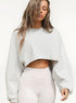 A woman with wet-look hair wearing a cream cropped sweatshirt with oversized sleeves and white leggings against white background
