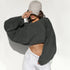 A woman wearing a charcoal cropped sweatshirt and white sweatpants adjusts her beige baseball cap against white background