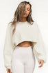 A woman with damp-look hair wearing a cream cropped sweatshirt with balloon sleeves and white high-waisted leggings against white background