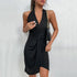 Woman wearing black halter wrap mini dress with plunging neckline and side tie detail, styled with gold chain purse