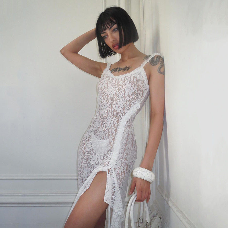 White lace dress with spaghetti straps and high side slit, worn by a woman with a short black bob hairstyle and tattoos, standing against a white wall