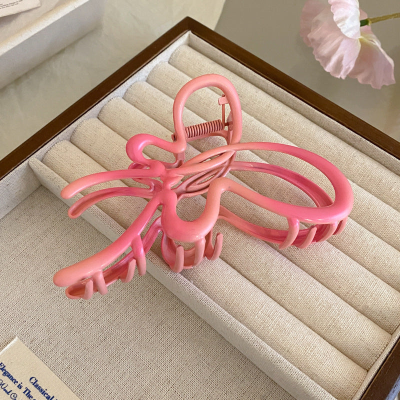 A large pink acrylic butterfly-shaped hair claw with an intricate cut-out design placed on a beige jewelry box.