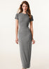 A woman confidently posing in a light gray short-sleeved maxi dress, accessorized with a necklace and bracelet.