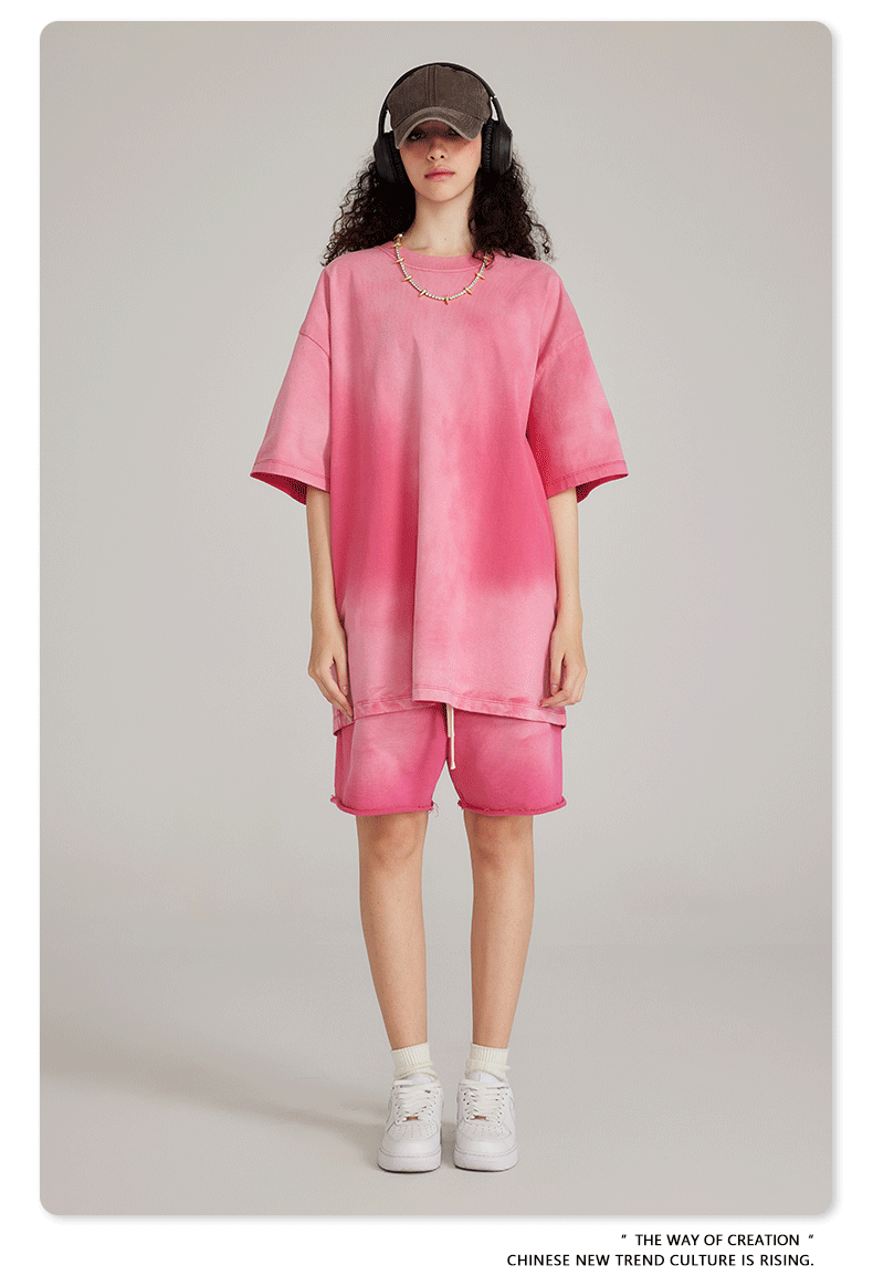 Model wearing pink t-shirt and matching shorts set with cap, headphones, beaded necklace, white socks and sneakers against cream background