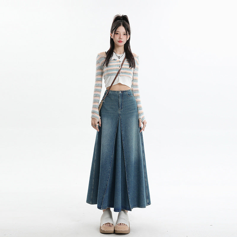 A woman posing in pastel striped crop cardigan and high-waisted denim maxi skirt with center pleat, styled with platform sandals and crossbody bag 
