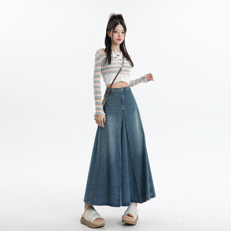 A woman wearing striped pastel cardigan with crop top, denim maxi skirt with front panel design, platform sandals, and small crossbody bag