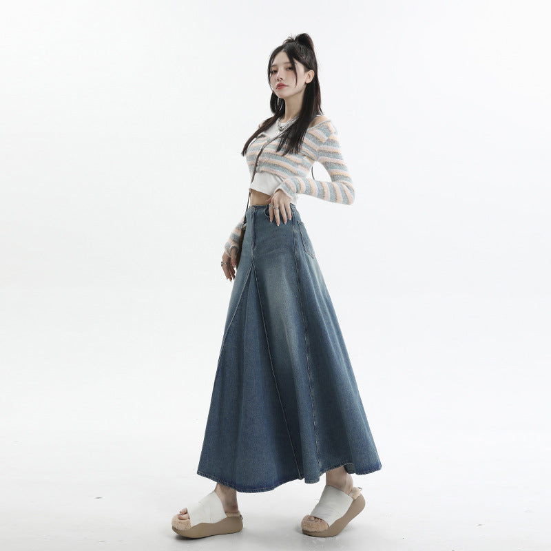 A woman in three-quarter pose wearing pastel striped crop cardigan, pleated denim maxi skirt, platform sandals, and silver jewelry