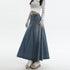 Close-up of denim maxi skirt with center pleat design paired with pastel striped crop cardigan and platform sandals, showing detail of high-waisted silhouette