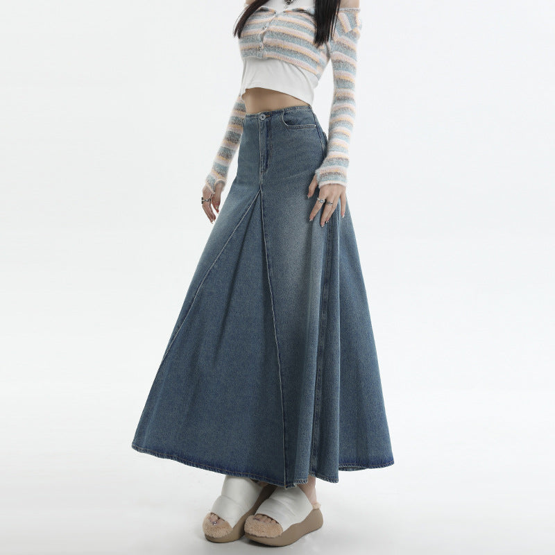 Close-up of denim maxi skirt with center pleat design paired with pastel striped crop cardigan and platform sandals, showing detail of high-waisted silhouette