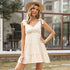 A woman is standing confidently in beige short tiered dress with tie straps, styled with straw boater hat, dainty necklace and seashell bracelet
