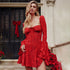 A woman wearing a red lace mini dress with corset bodice and bell sleeves posing in front of a dark wooden door with holiday decorations