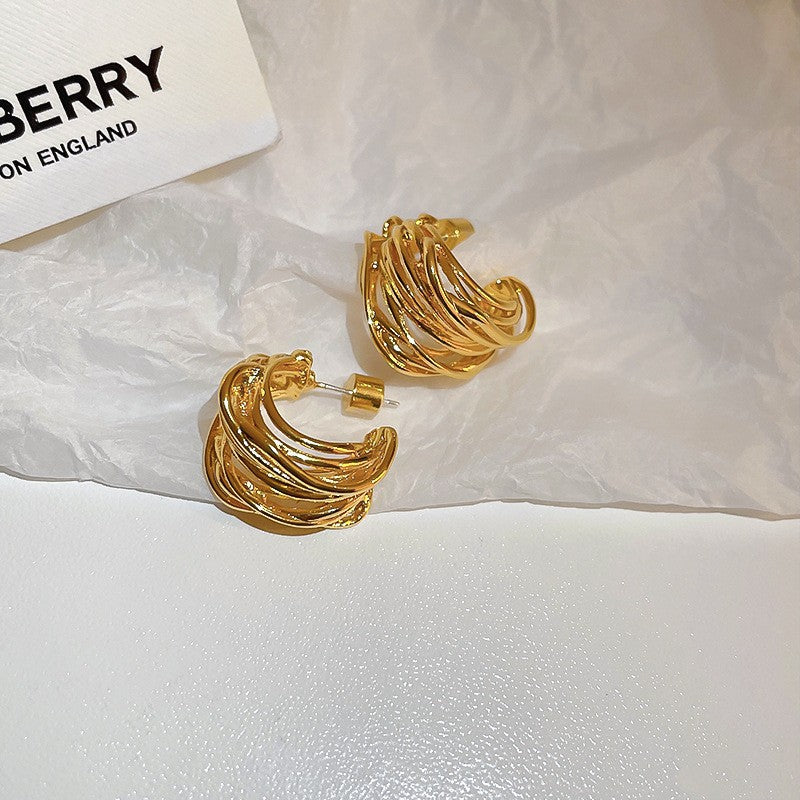Gold Twisted Hoop Earrings – Elegant gold hoop earrings with a layered, twisted wire design, displayed on crinkled paper