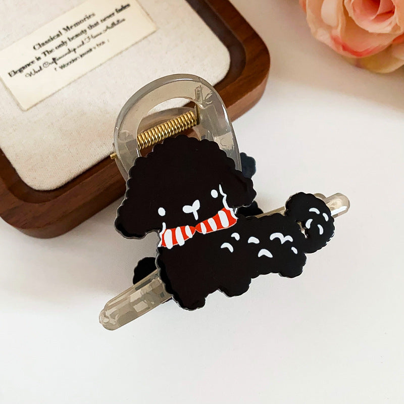 A playful black poodle-shaped hair claw with a red and white striped scarf, secured on a transparent clip.