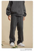 Front view of person wearing dark grey tracksuit with silver watch and white sneakers on beige background