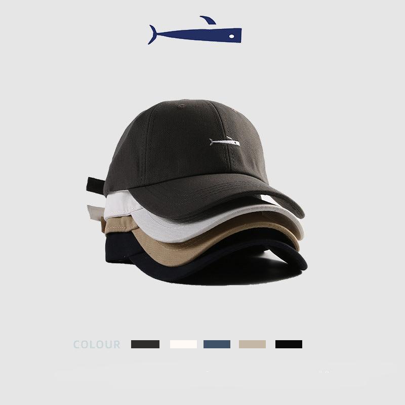 Stacked baseball caps in various colors featuring a minimalist fish embroidery