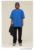 Man with short dreadlocks wearing royal blue oversized t-shirt, black sweatpants, navy baseball cap and silver chain necklace, holding black jacket