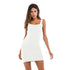 A woman wearing a white ribbed mini dress with square neckline and scalloped trim posing directly facing camera against minimalist backdrop
