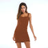 A woman wearing a brown ribbed mini dress with scalloped neckline and straight straps standing against a simple white photography background