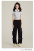 Model with curly dark hair wearing light gray crop top, black cargo pants with zippered pockets, white headphones and cream sneakers on neutral background